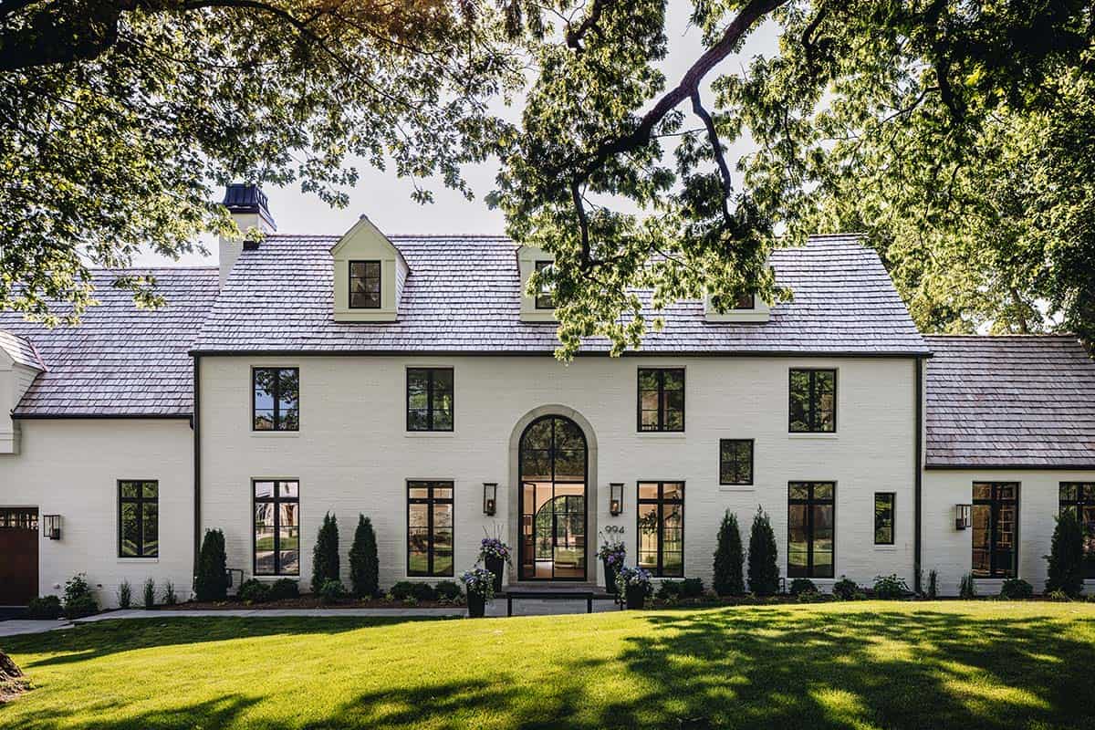 Front facade of white brick home framed by mature oak tree with arched entry and dormers
