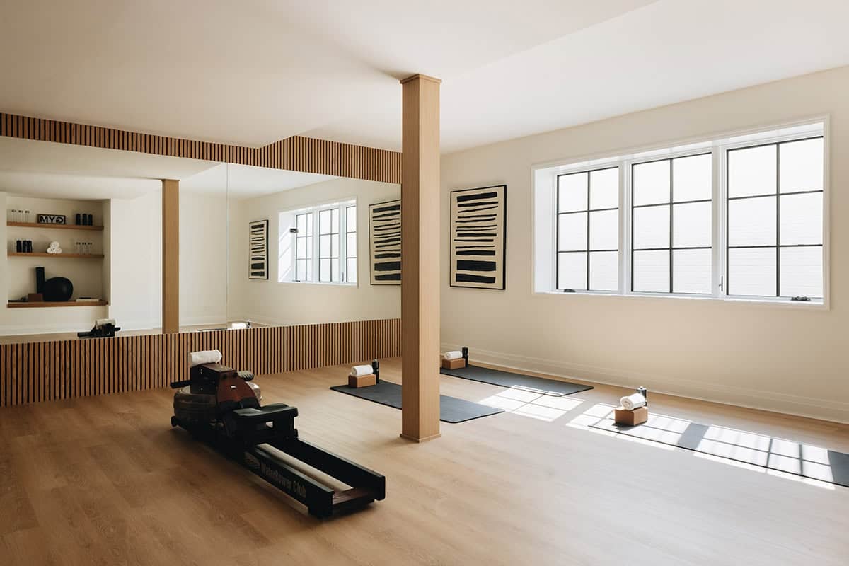 Home gym with slatted wood accent wall, mirrors, rowing machine, and yoga mats near large windows