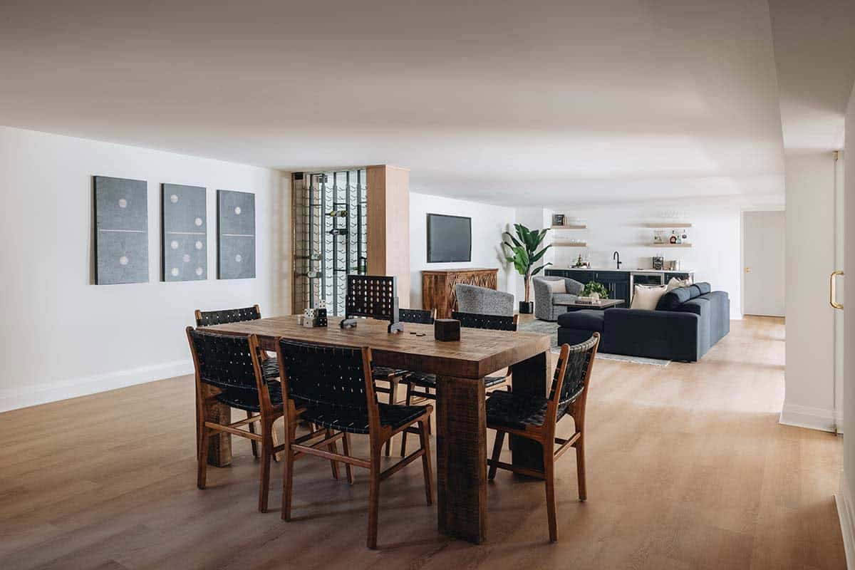 Game room with wooden dining table, woven leather chairs, domino wall art, and bar lounge beyond