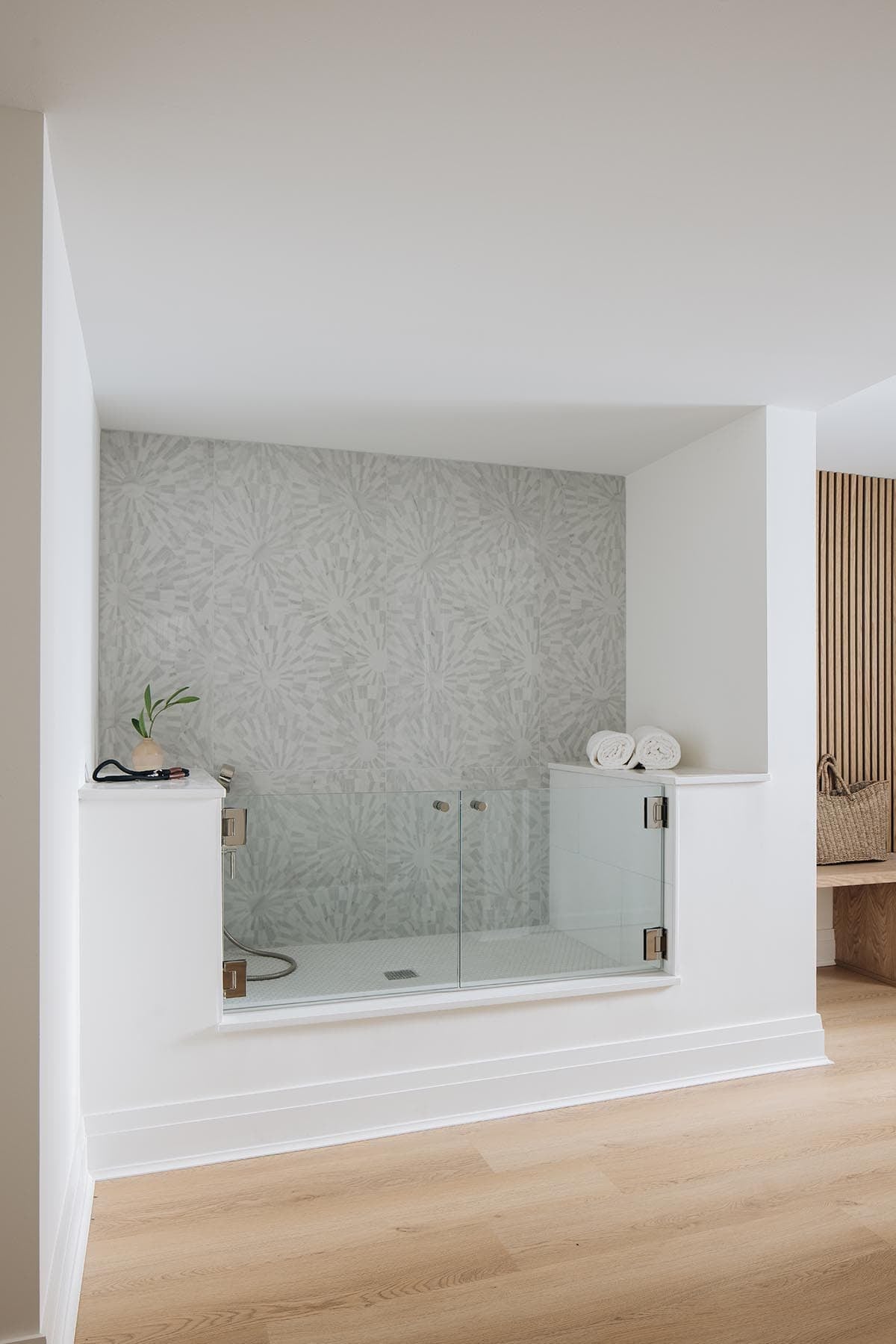 Sunken glass-enclosed cold plunge tub with starburst mosaic tile wall and rolled towels
