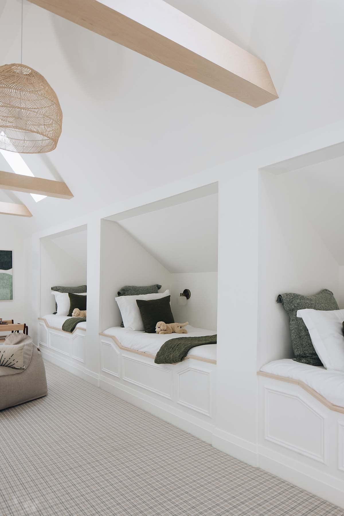 Row of built-in bunk alcoves under vaulted ceiling with wood beams and woven pendant lights
