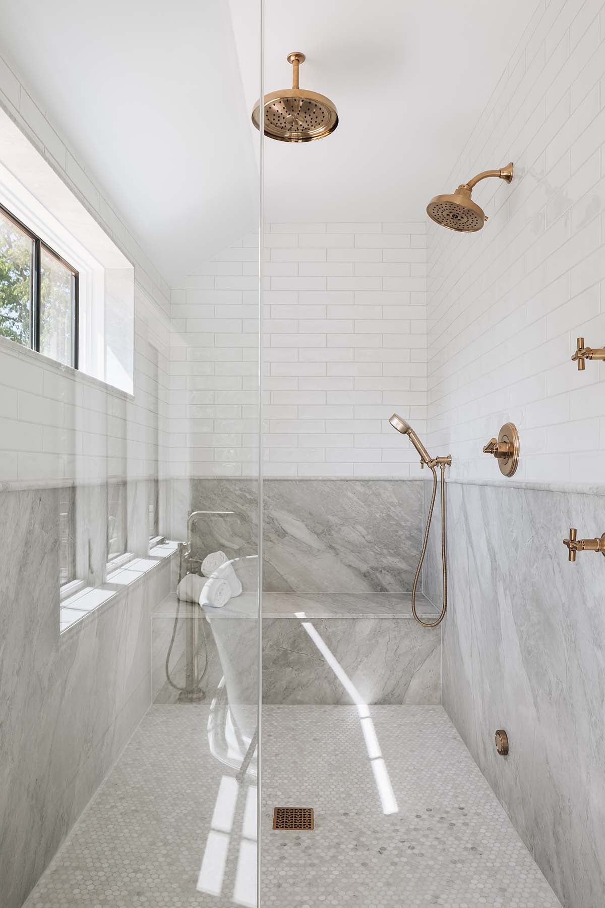 Marble-tiled walk-in shower with dual brass rainfall showerheads and built-in bench seating