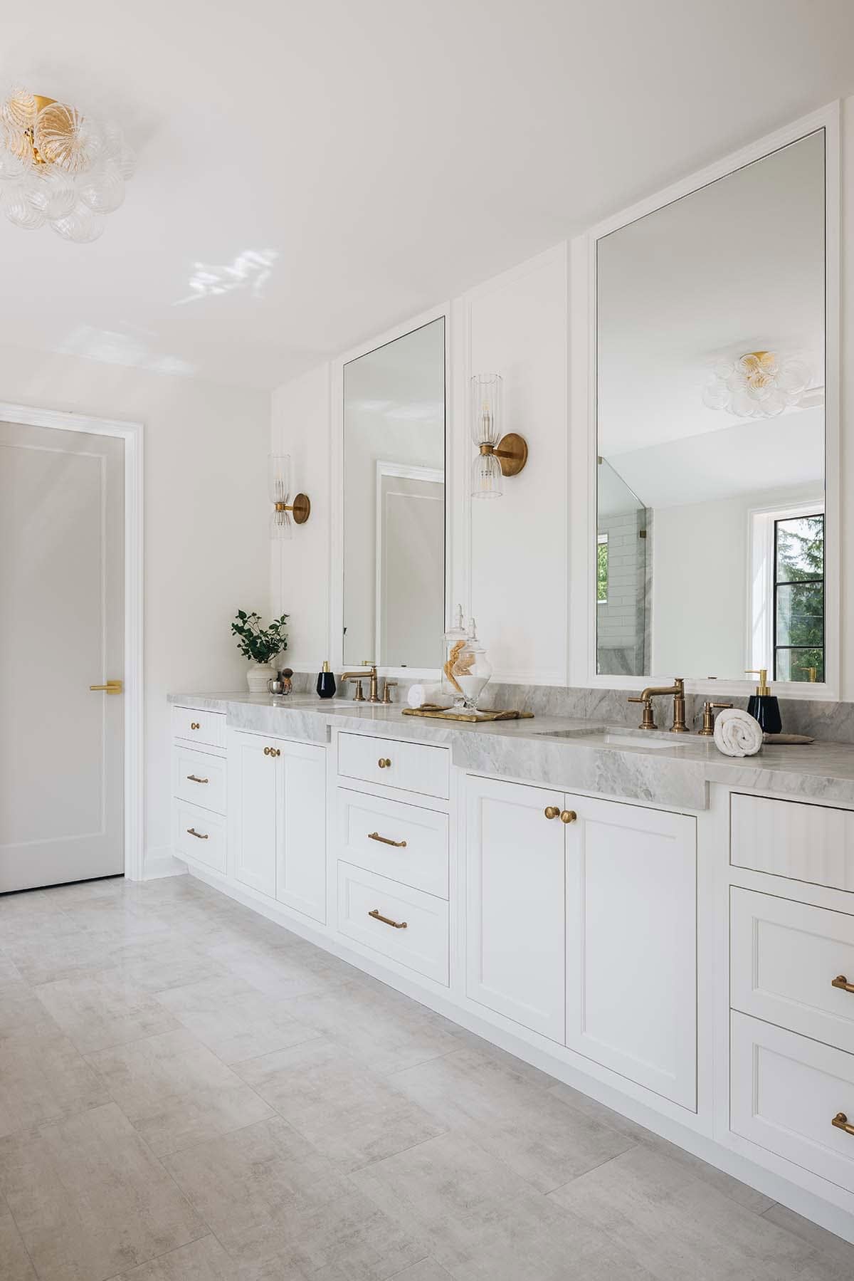 Long double-sink bathroom vanity with marble countertop, brass fixtures, and tall mirrors