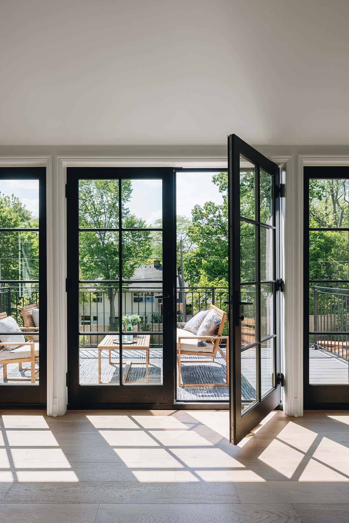 Open French doors leading to deck with outdoor seating and treetop views