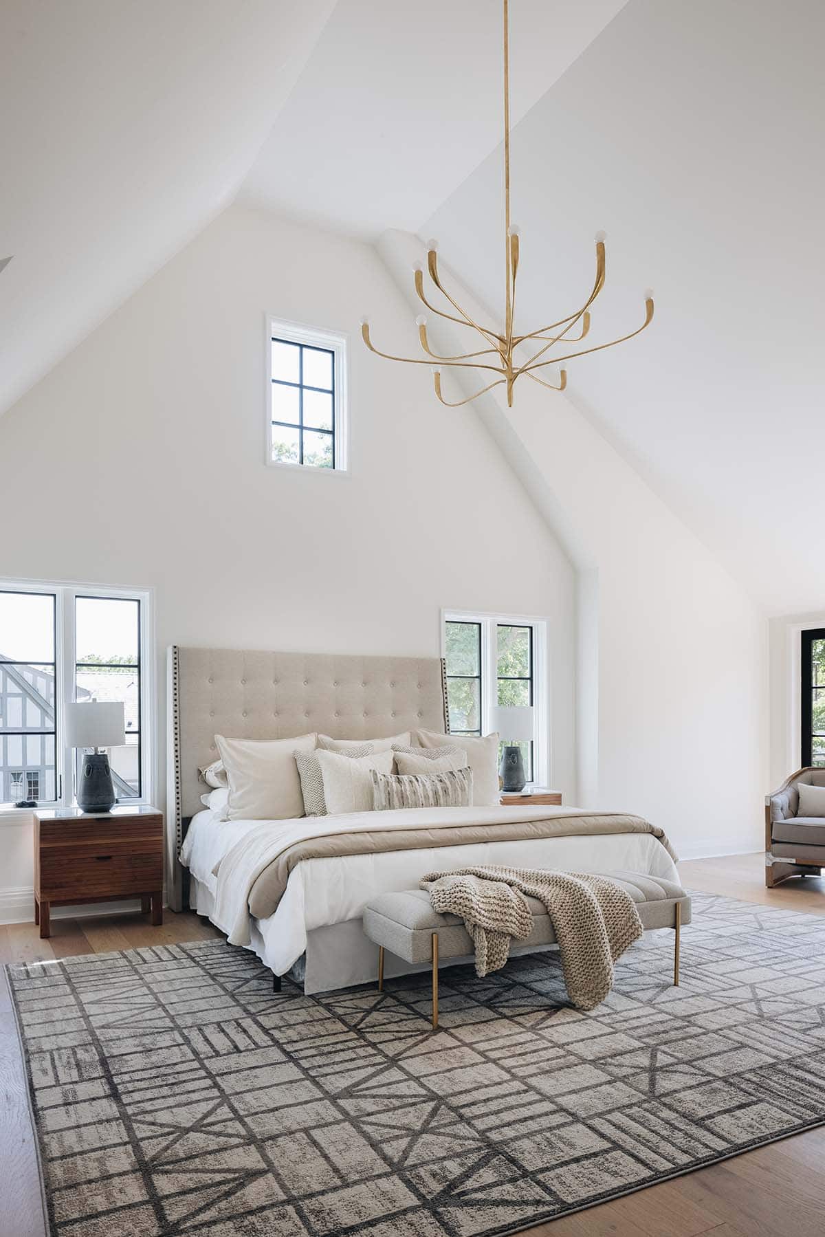 Primary bedroom with tufted headboard, brass chandelier, patterned rug, and cathedral ceiling