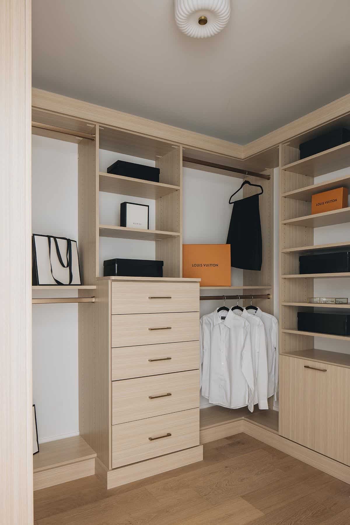 Walk-in closet with light oak built-ins, drawer chest, and designer boxes on open shelving