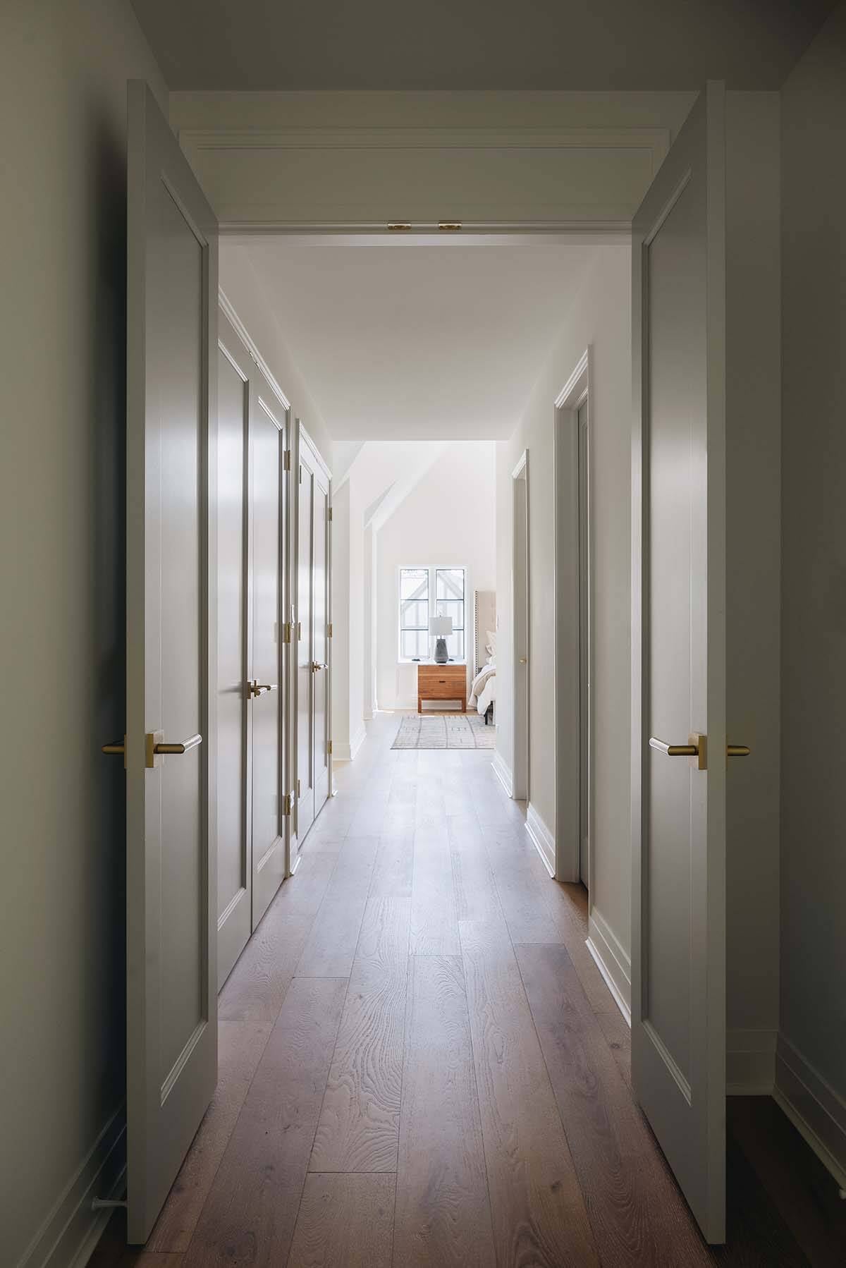 Hallway view through open doors toward bedroom with herringbone-look wood flooring