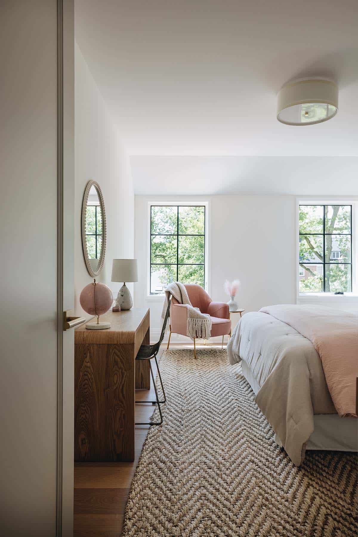 Girl's bedroom nook with pink accent chair, oval mirror, wood desk, and herringbone jute rug