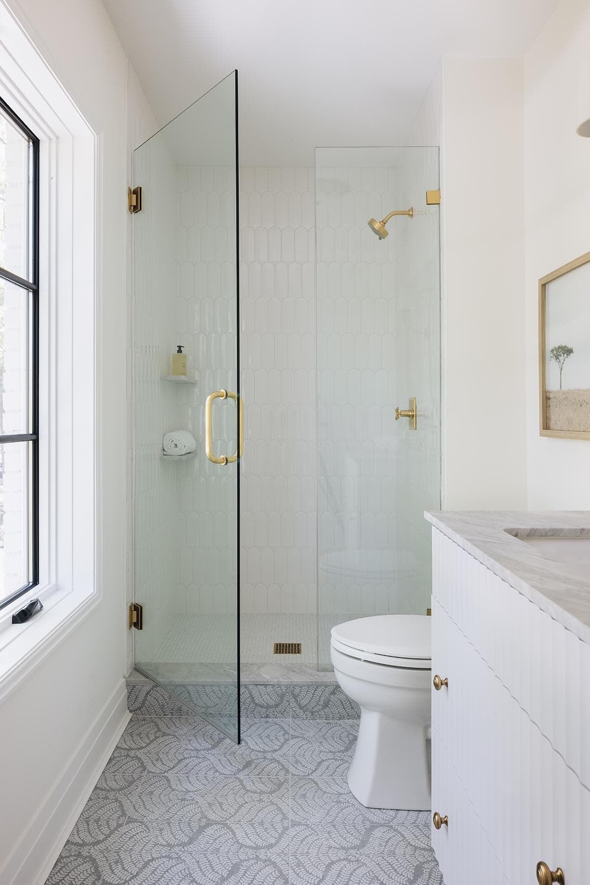 Narrow bathroom with scalloped tile shower, brass hardware, and patterned leaf tile flooring