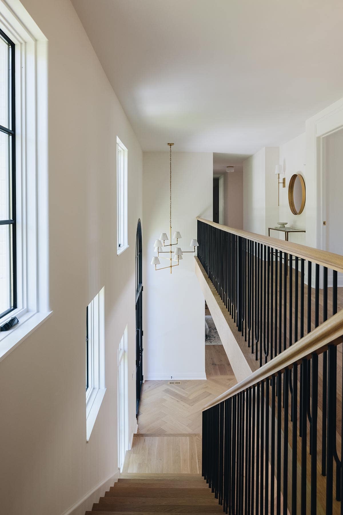 Upper landing staircase with black iron balusters, brass chandelier, and herringbone floor below