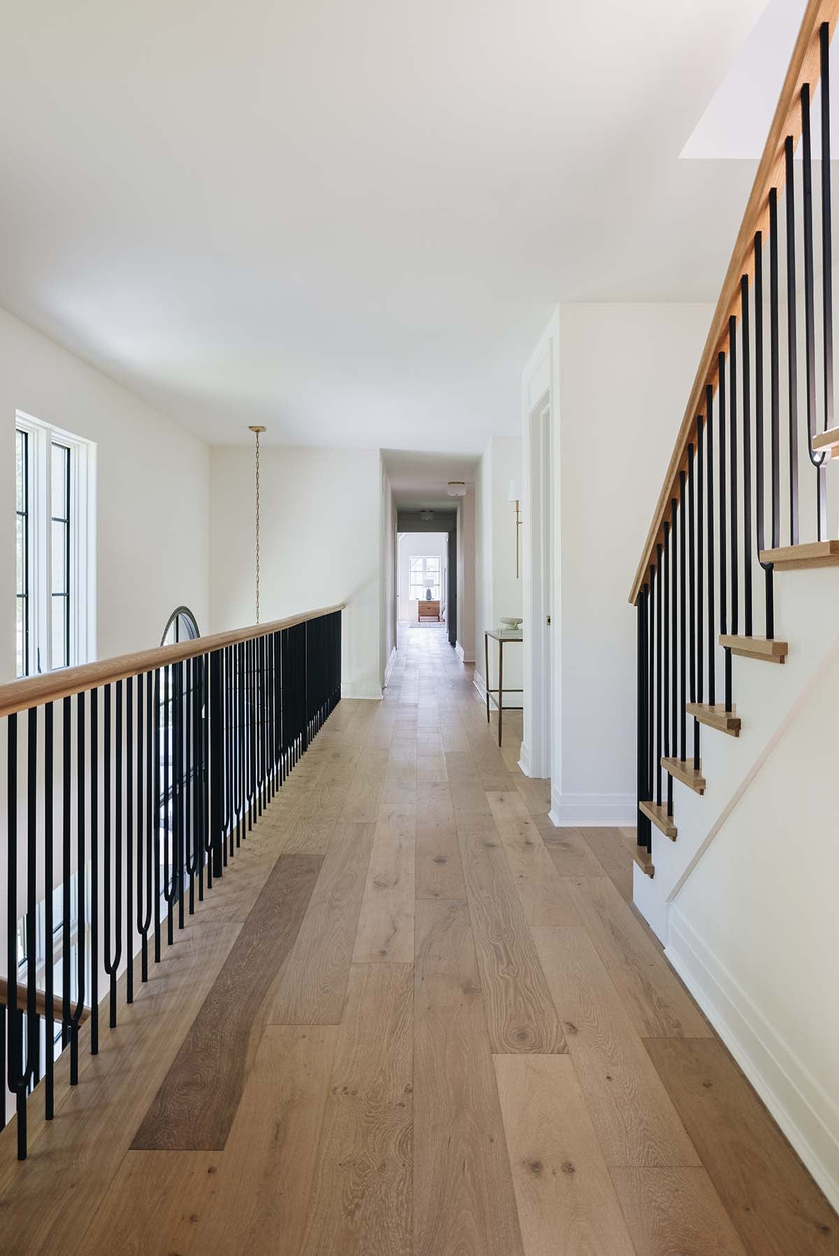 Upstairs hallway with black spindle railing, wood-capped staircase, and light oak flooring