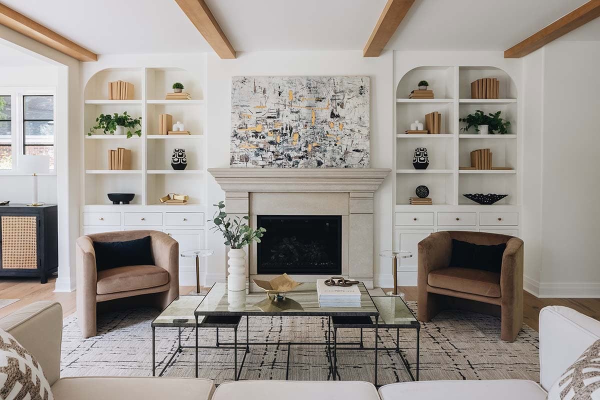 Living room with stone fireplace, arched built-in bookshelves, and camel leather barrel chairs