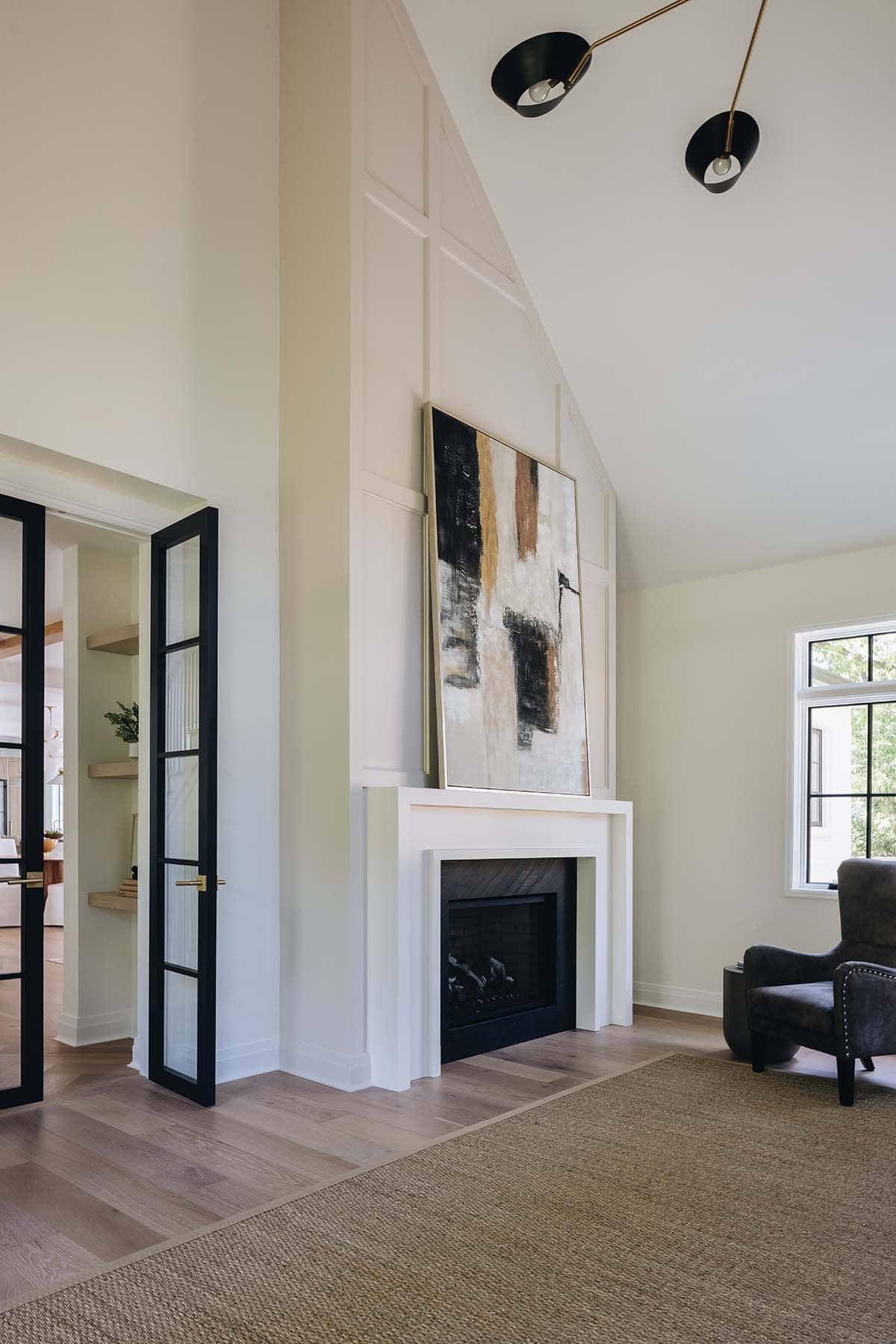Living room fireplace with abstract art, black double-cone sconces, and glass-paneled door