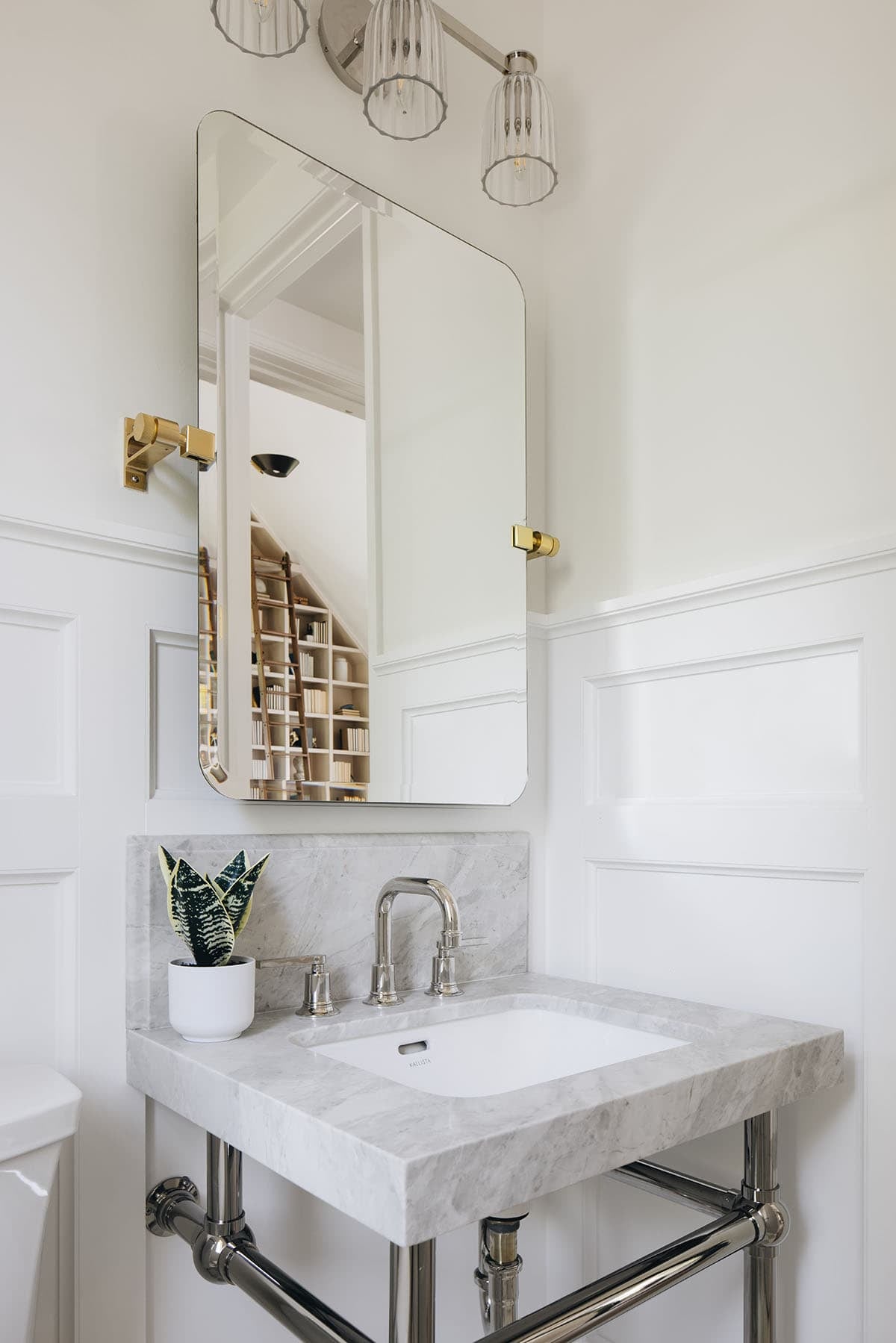 Powder room with tilting rectangular mirror, brass hardware, and marble console sink