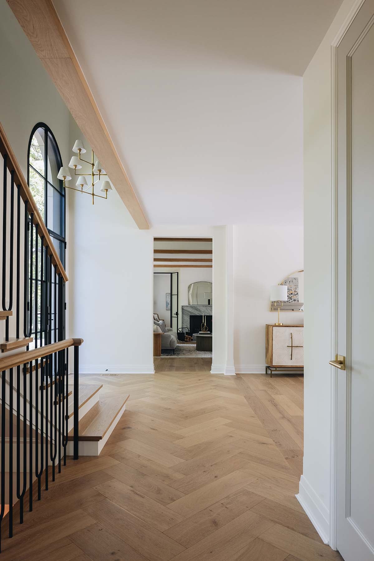 Hallway view toward living room with stone fireplace and herringbone wood flooring