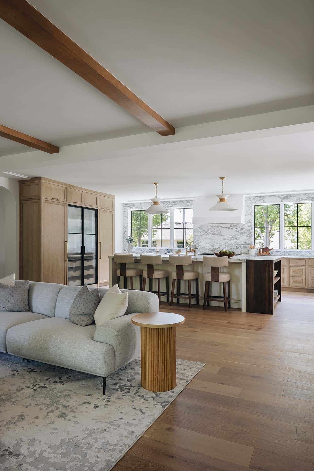 Open living and kitchen area with gray sectional, wine fridge, and marble backsplash island