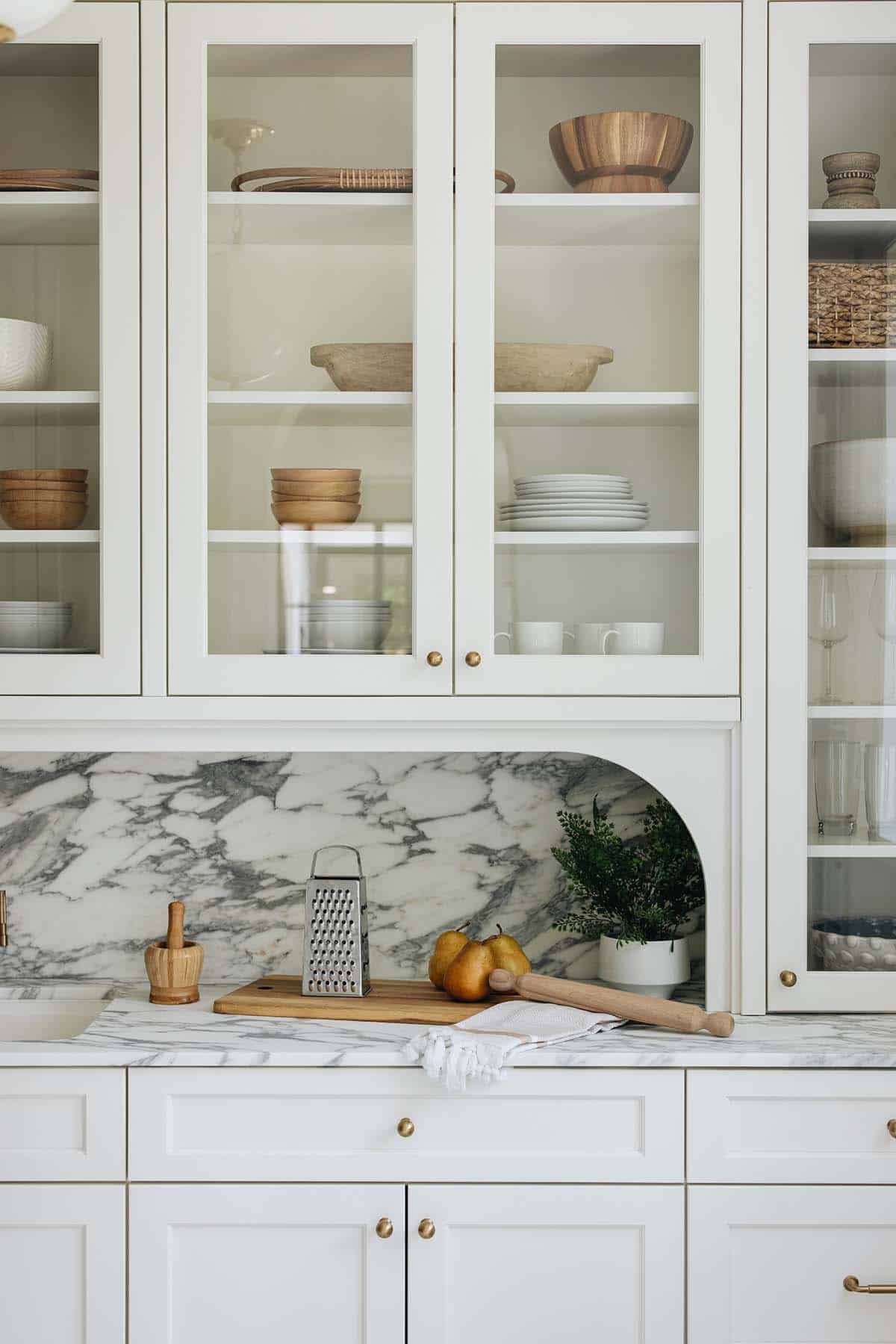 Close-up of glass-front cabinet displaying dishware above arched marble backsplash niche