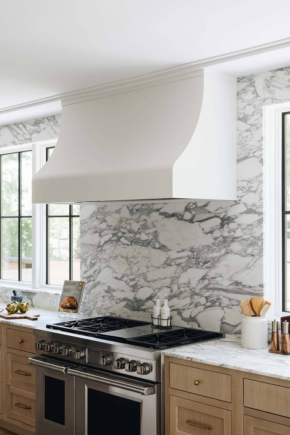 Range hood with full-slab marble backsplash, gas cooktop, and brass utensil canister