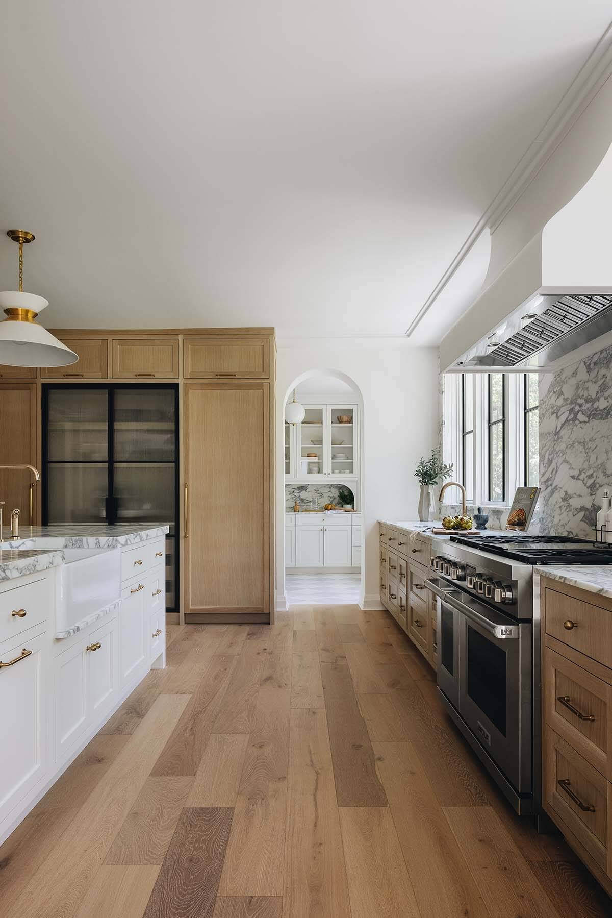 Galley kitchen view with white island, oak cabinetry, marble backsplash, and arched pantry doorway