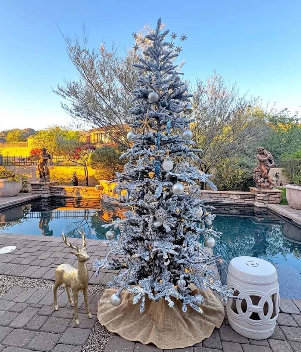 Flocked Christmas tree with starfish topper and blue coastal ornaments beside a pool