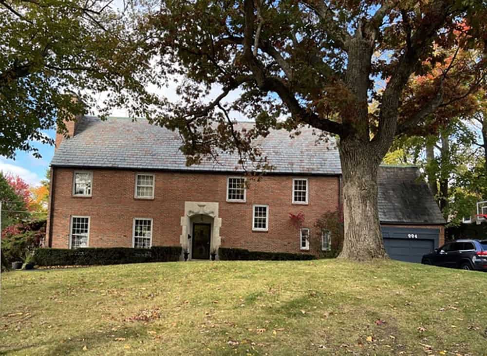 Front exterior of brick English manor home shaded by mature oak tree
