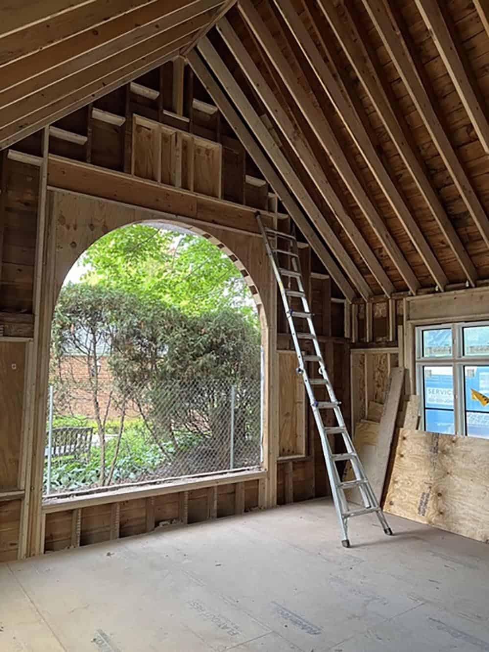 Framed addition under construction with arched window opening to yard