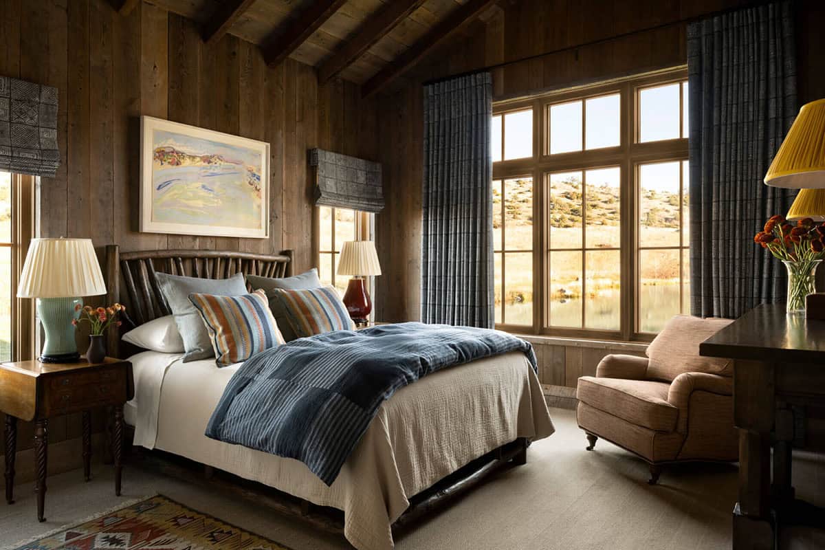 Bedroom with wood-paneled walls and large windows overlooking the pond