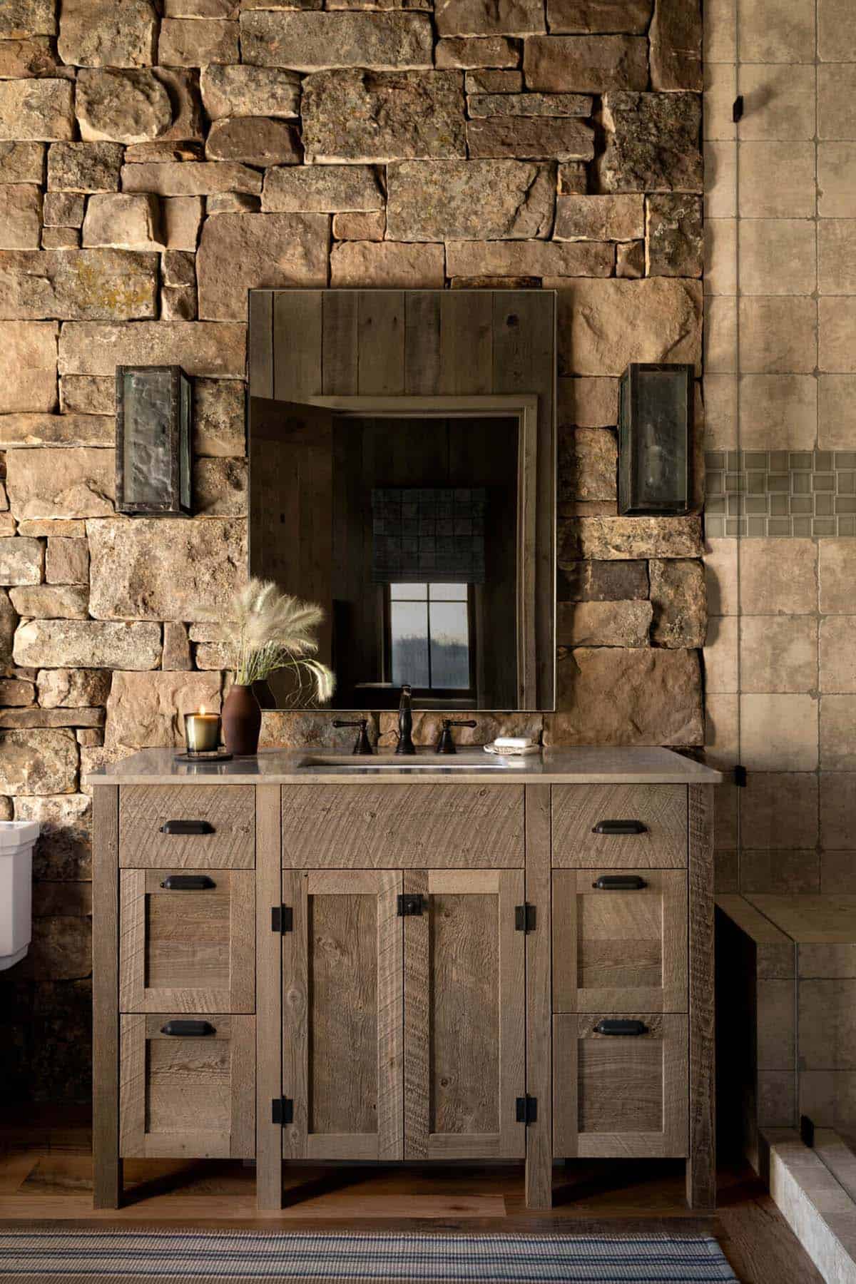 Bathroom vanity against a stacked stone wall with wood mirror