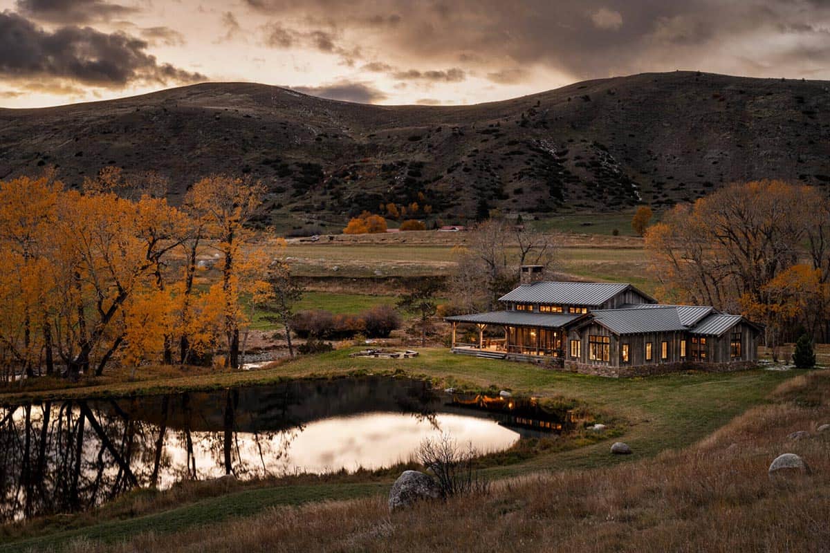 Aerial twilight view of Boulder Retreat Ranch beside a pond with autumn trees and Montana hills