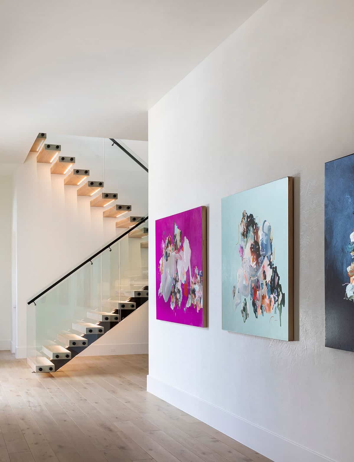 Floating staircase beside gallery wall of colorful abstract paintings