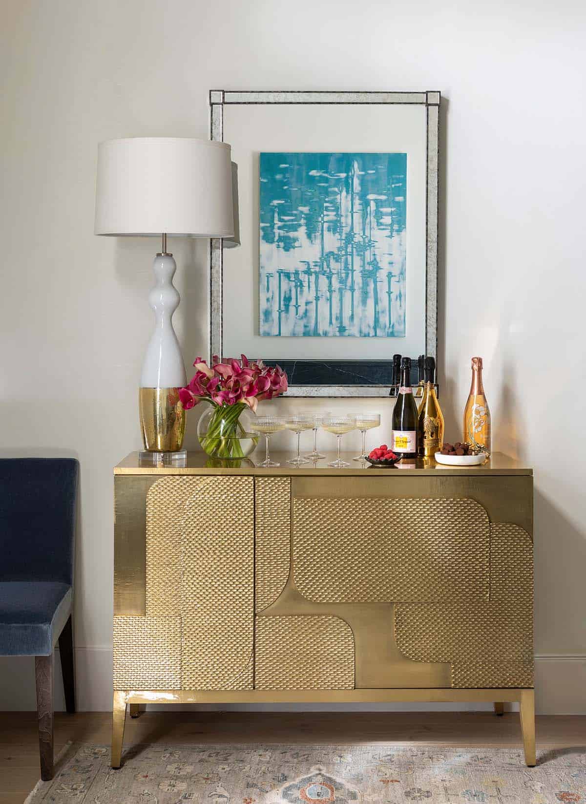 Gold textured bar cabinet with mirror, teal artwork, and champagne bottles