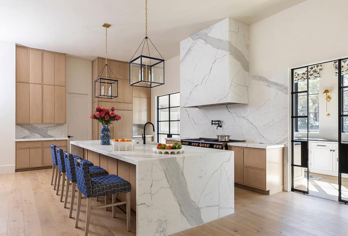 Kitchen with marble waterfall island, blue barstools, and glass lantern pendants