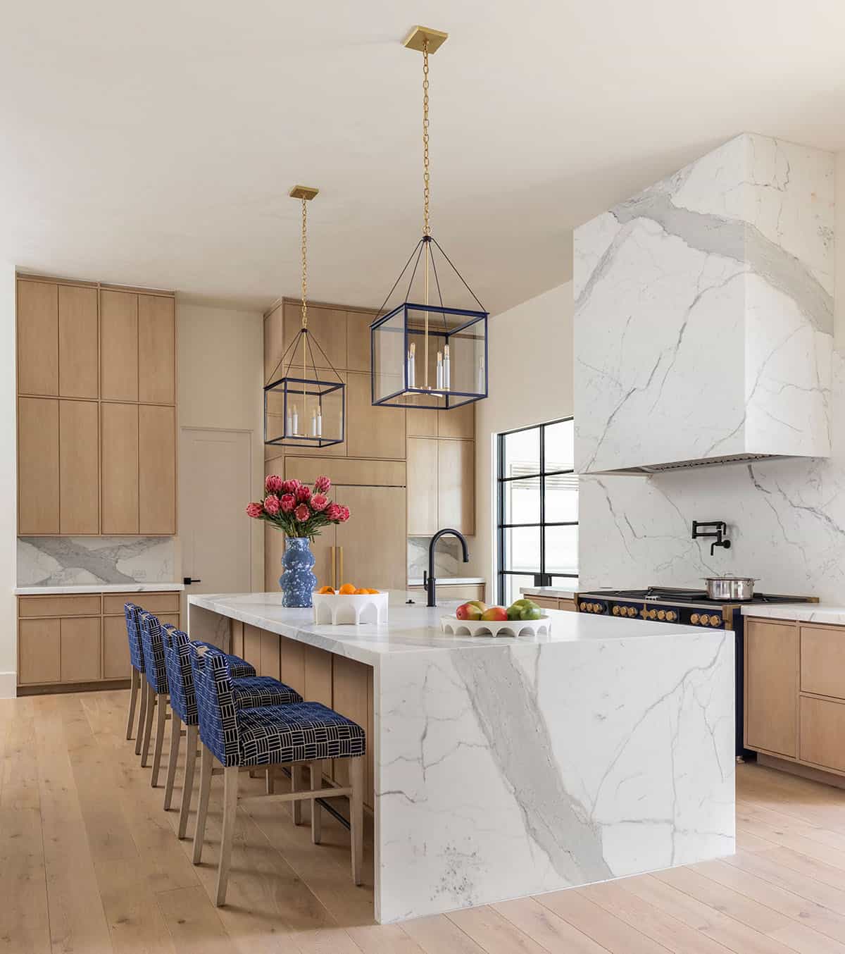Kitchen island with marble hood, navy pendant lights, and blue floral vase