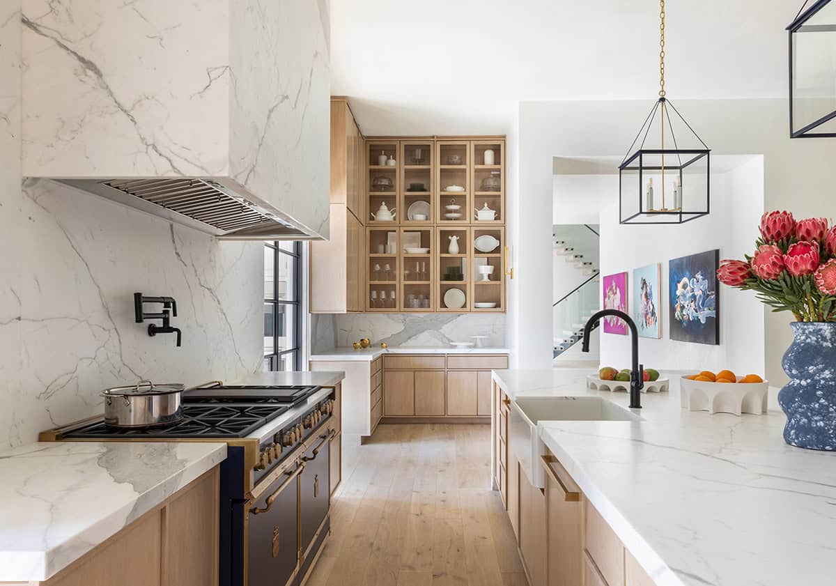 Kitchen view with marble range hood, glass-front cabinets, and gallery hallway