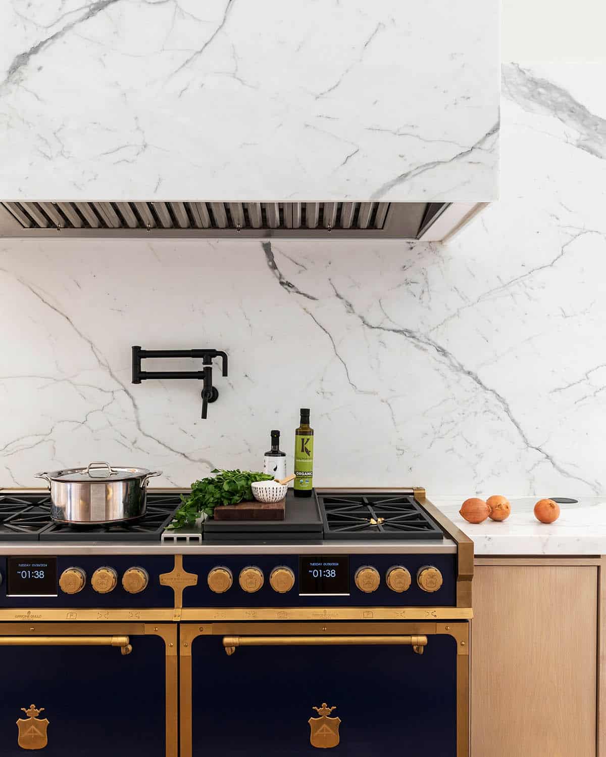 Close-up of navy and brass range with marble hood and pot filler