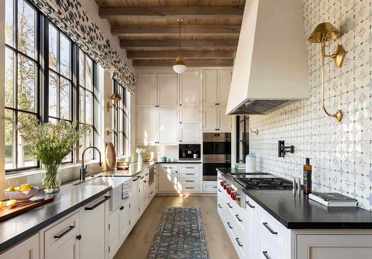 White galley kitchen with black countertops, wood beam ceiling, and tiled backsplash