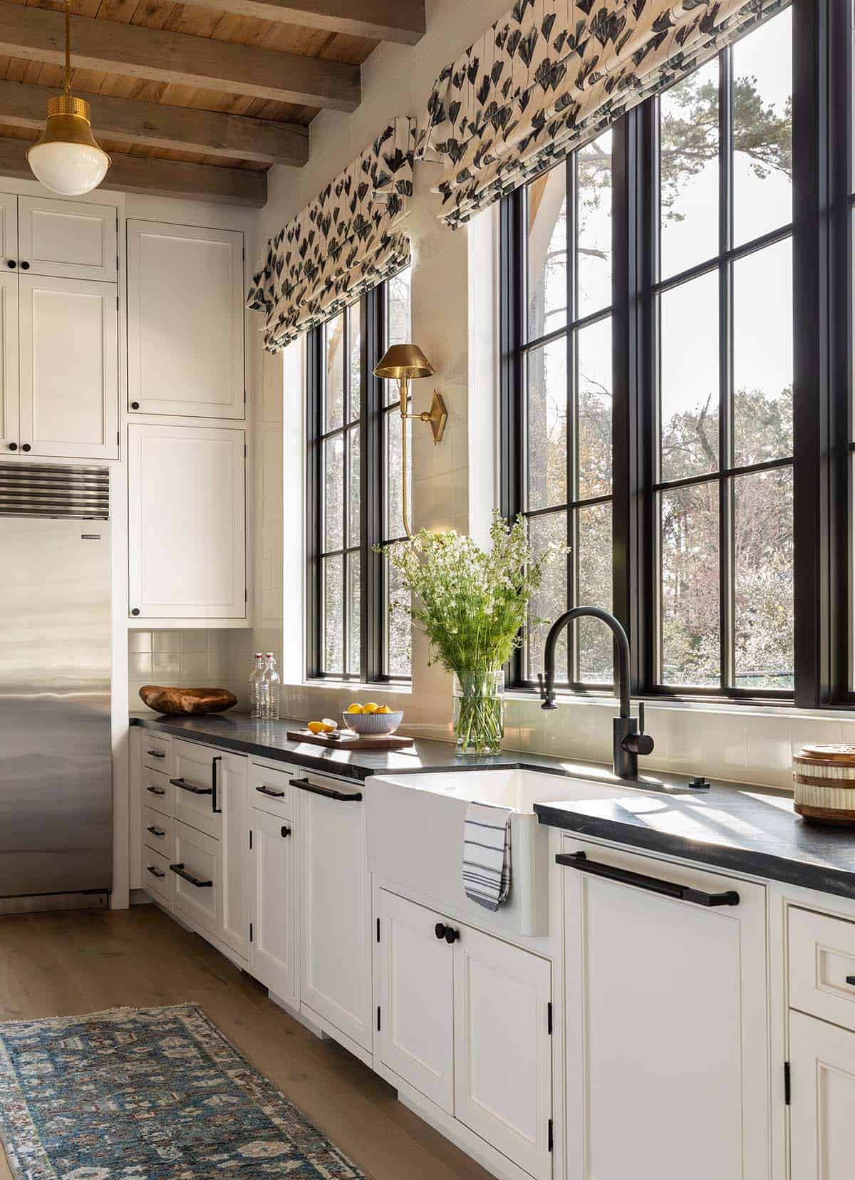 White kitchen sink area with steel windows overlooking wooded yard