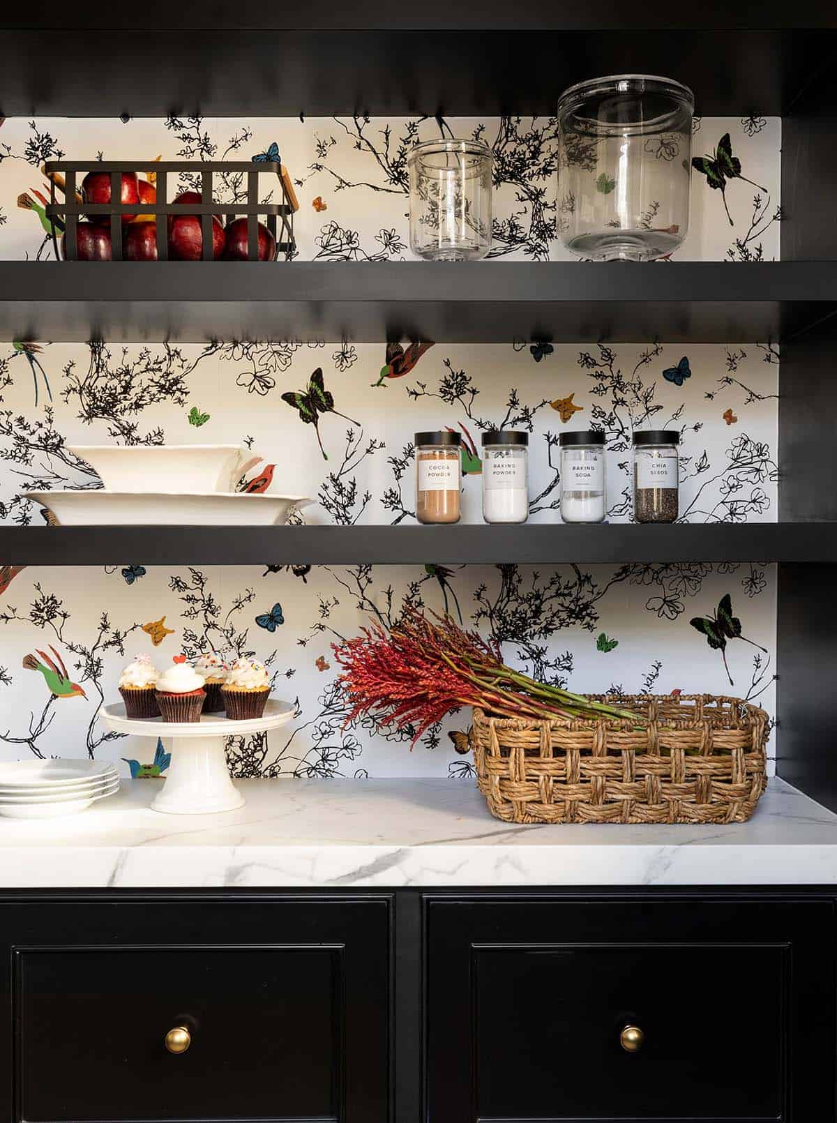 Black pantry shelves with bird wallpaper, labeled jars, and cupcakes