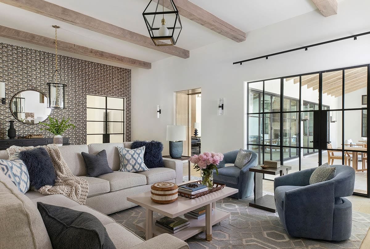 Living room with geometric wallpaper, neutral sofas, and blue swivel chairs