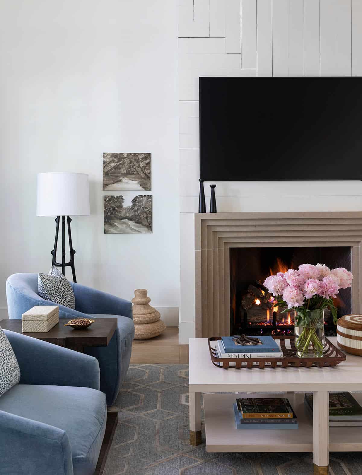 Living room fireplace with stone surround, blue chairs, and TV above mantel