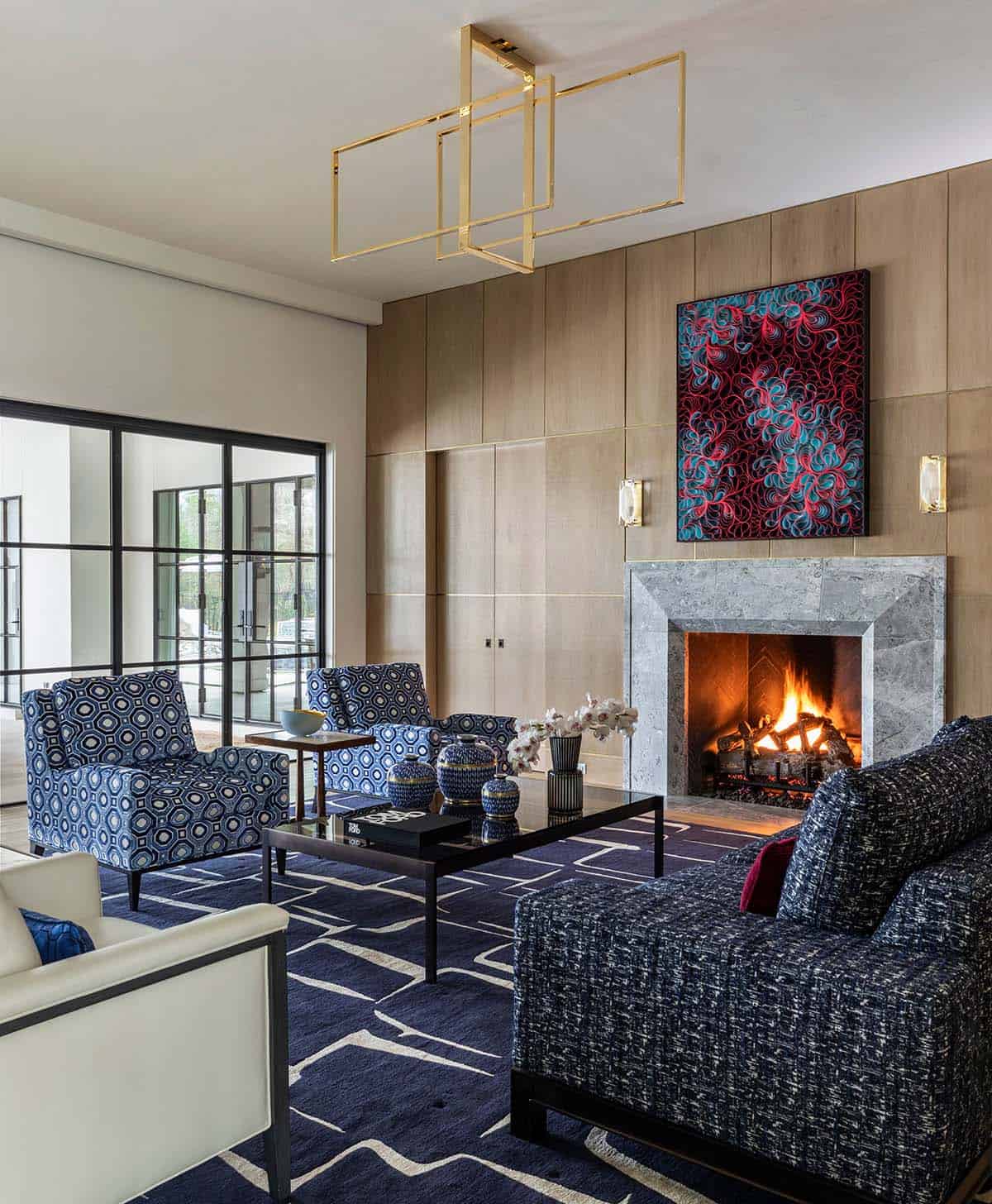 Living room fireplace with stone mantel, gold chandelier, and blue seating