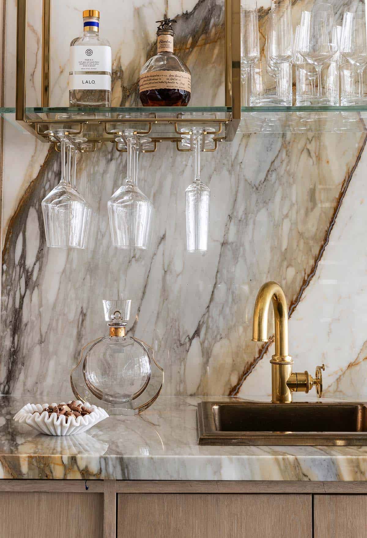 Close-up of marble wet bar with brass faucet and hanging wine glasses