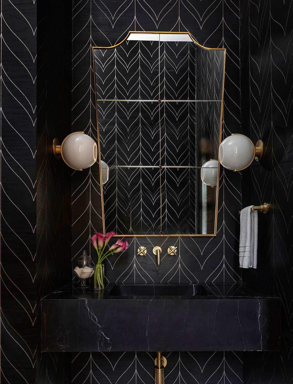 Black powder room with patterned wallpaper, brass mirror, and globe sconces