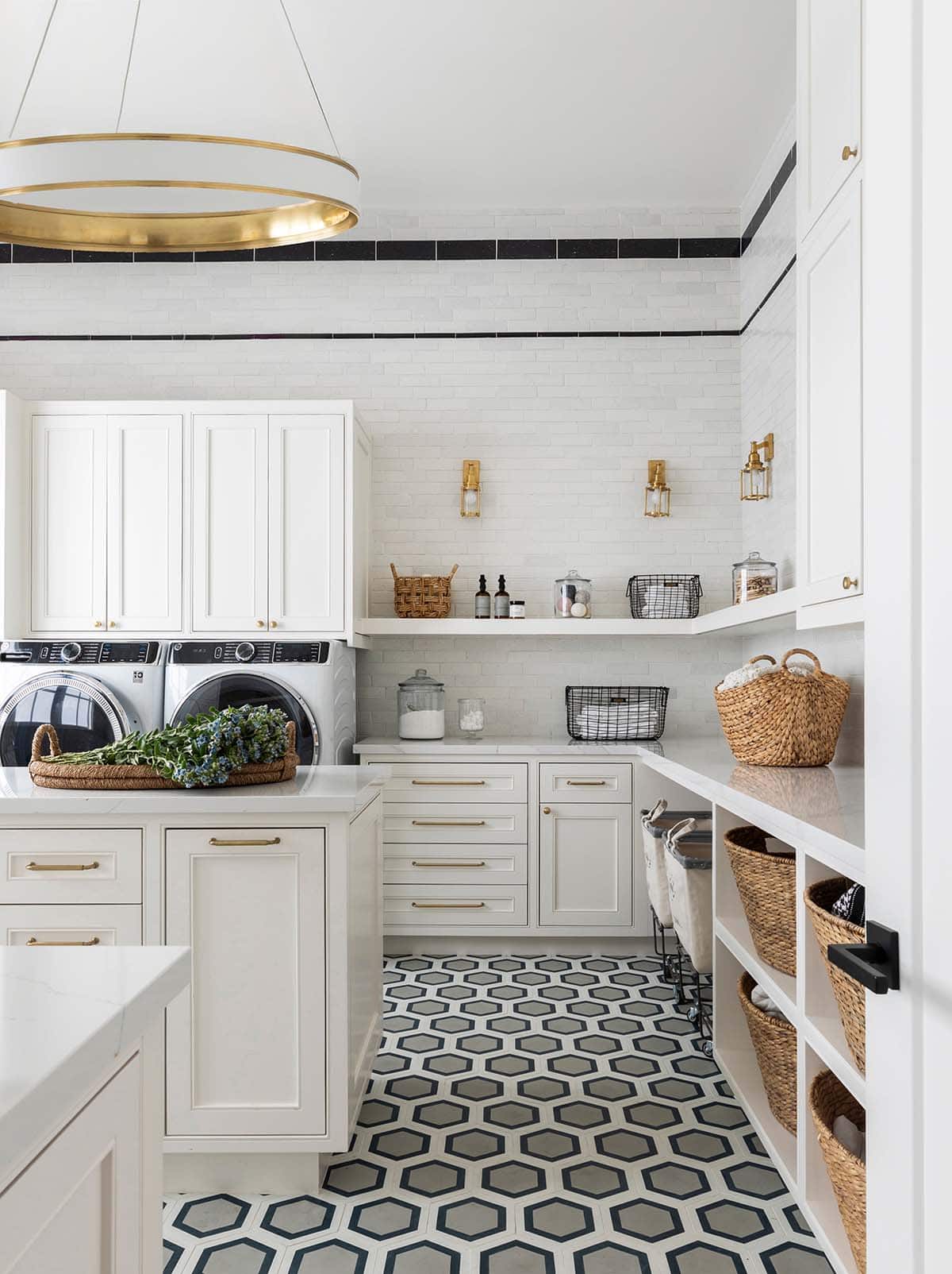 White laundry room with hexagon tile floor, brass sconces, and woven baskets
