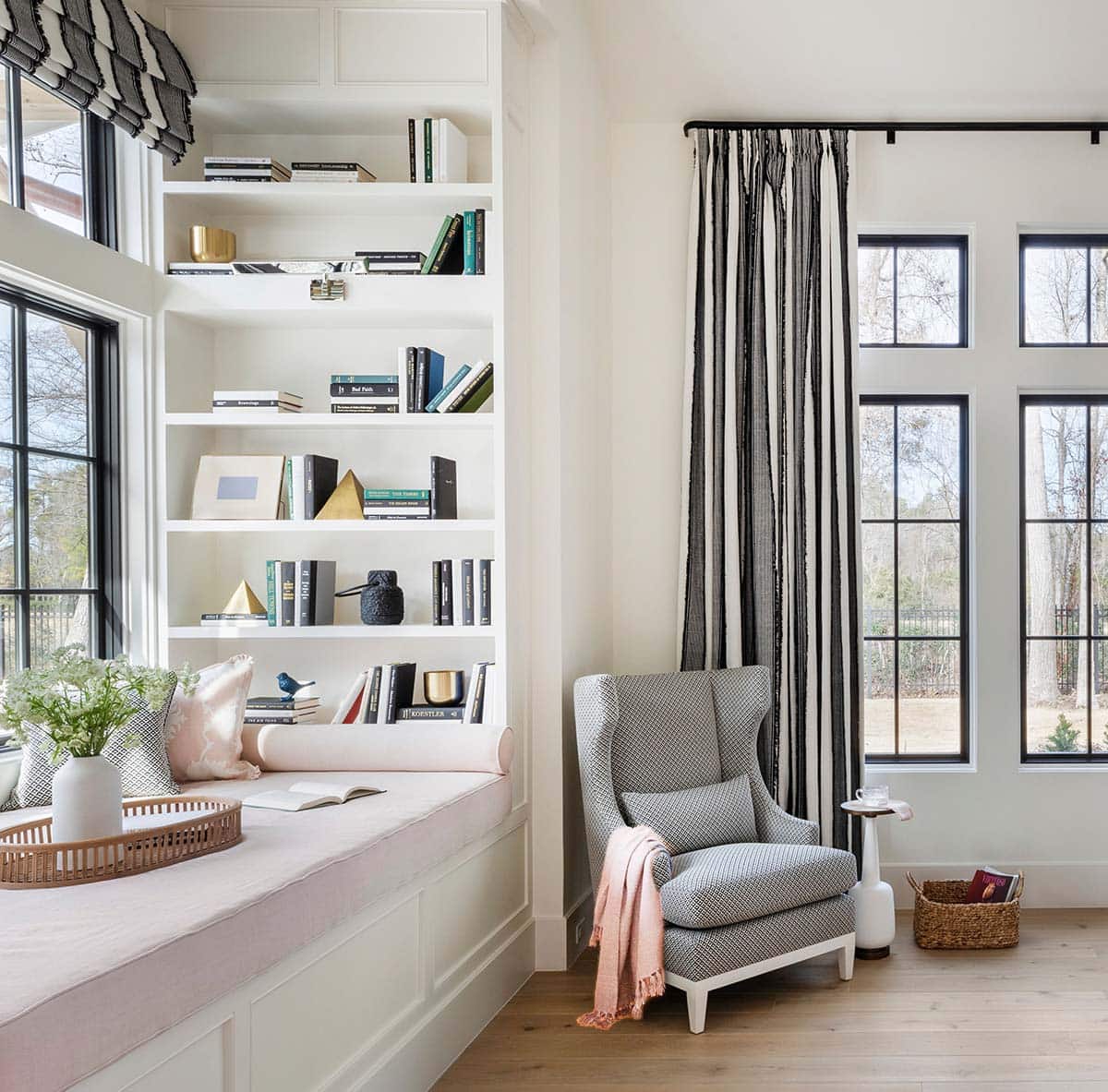 Window seat nook with pink cushion, bookshelf, and striped curtains