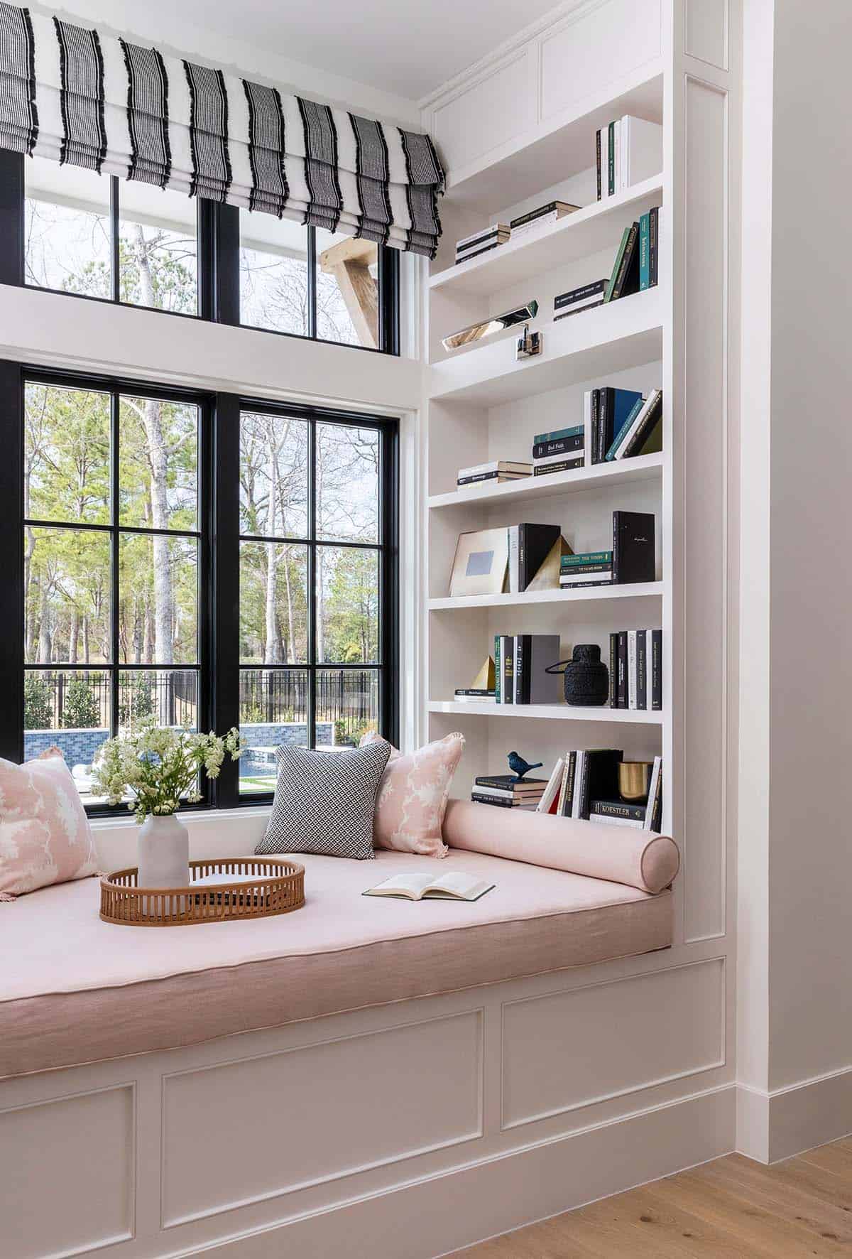 Pink window seat with bolster pillows and built-in bookshelf