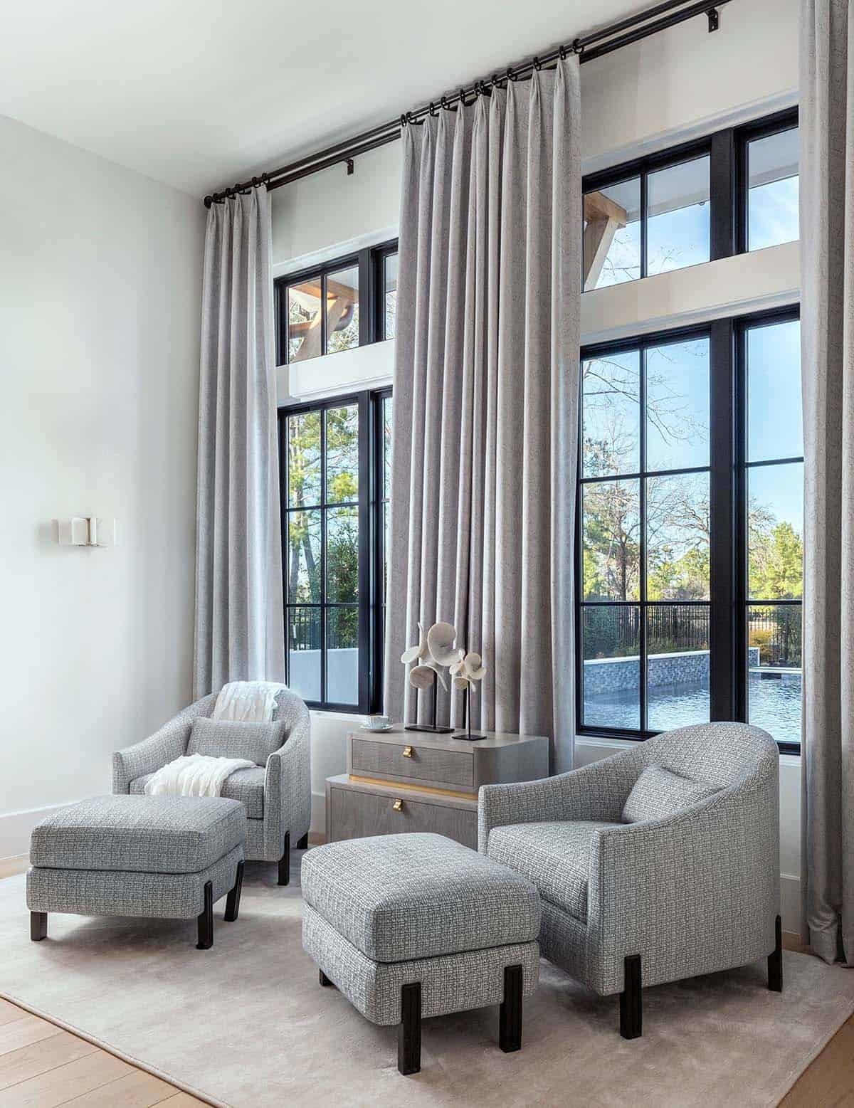 Sitting area with gray tweed chairs and floor-to-ceiling curtains overlooking pool