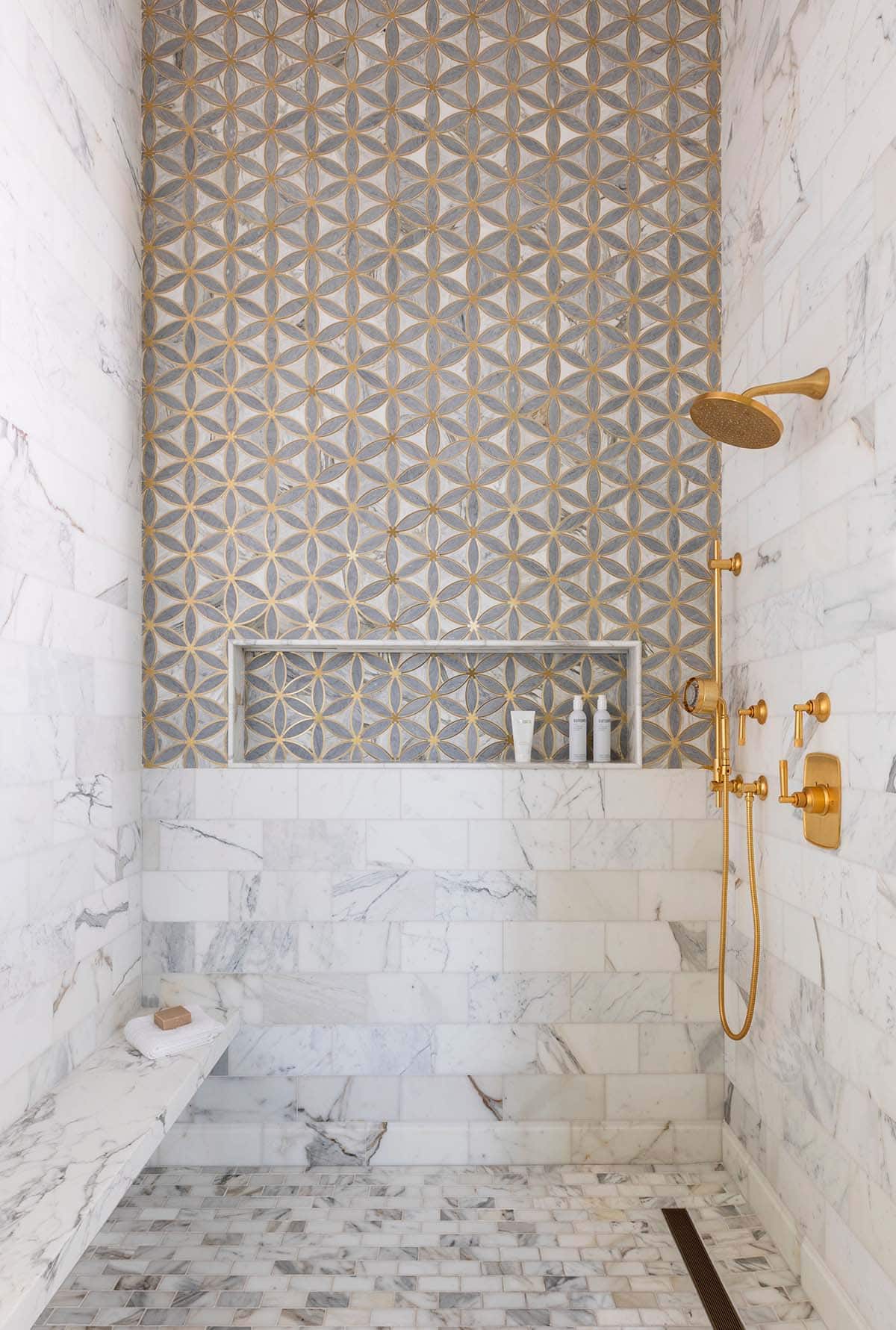 Marble shower with gold flower-pattern tile accent and brass fixtures