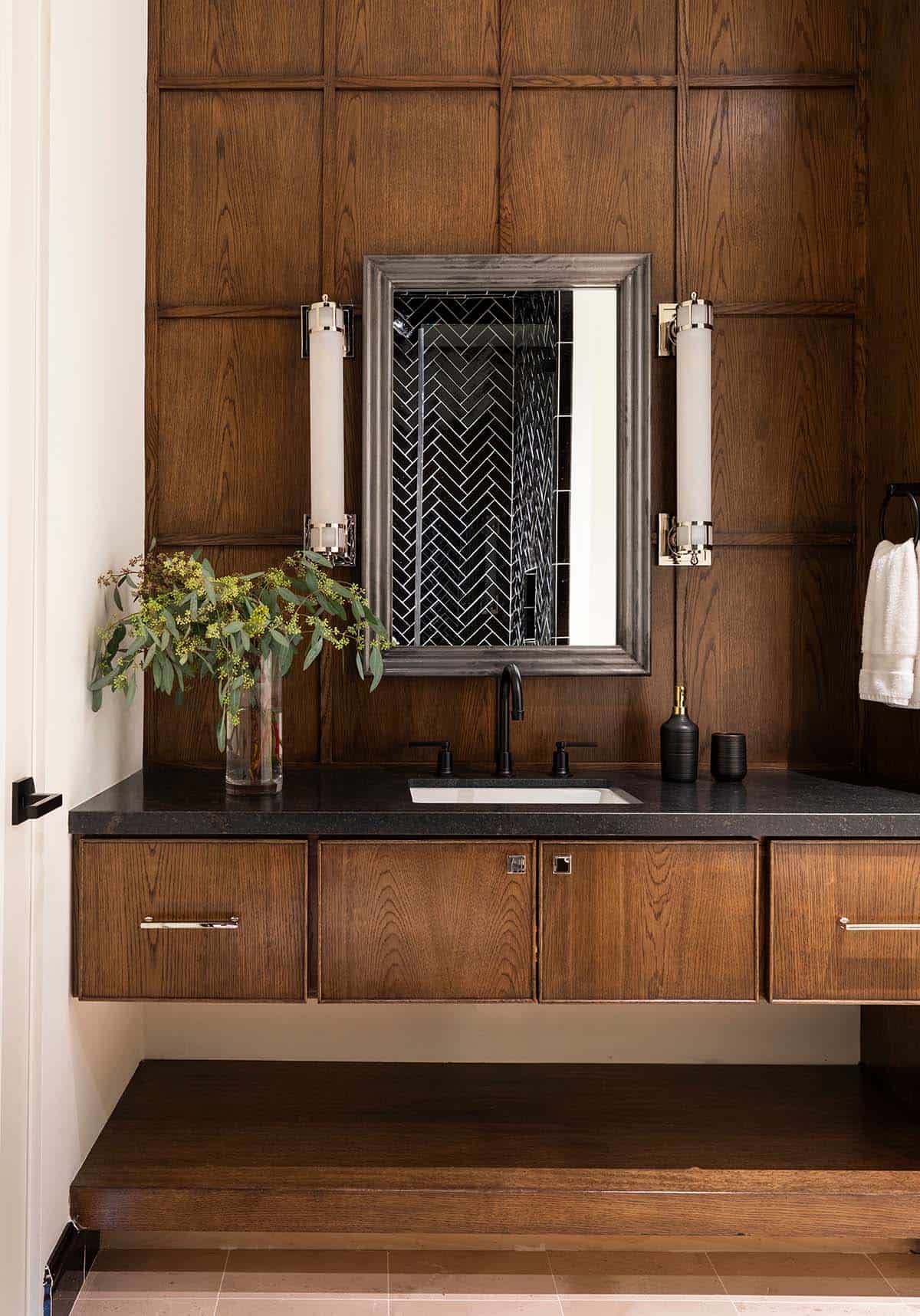 Wood-paneled powder room with black herringbone tile mirror reflection