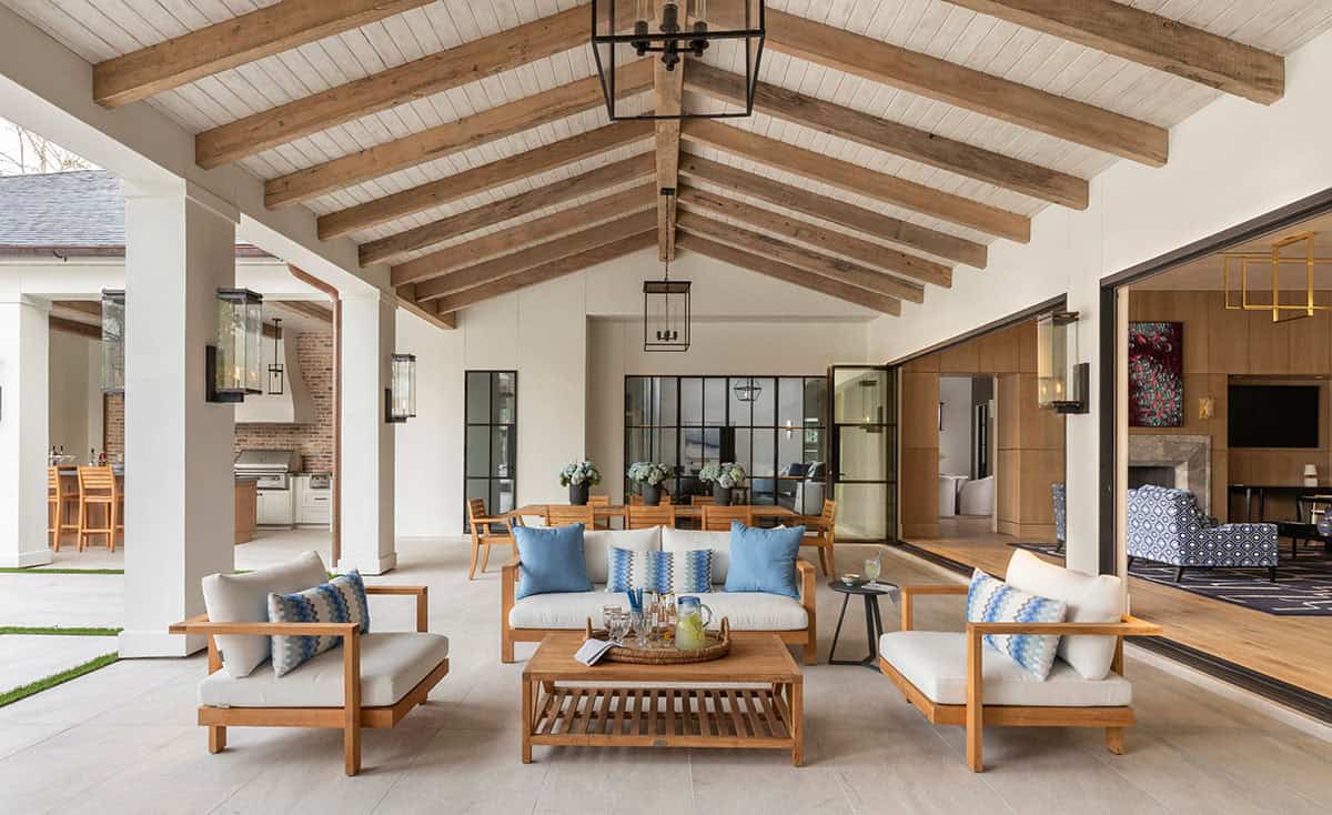Covered patio with wood beam ceiling, teak furniture, and blue pillows